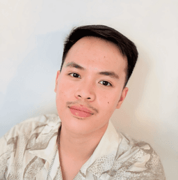 A man with black hair and beige shirt smiling at the camera