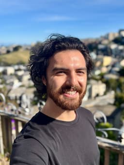 A man with black hair and black shirt smiling at the camera